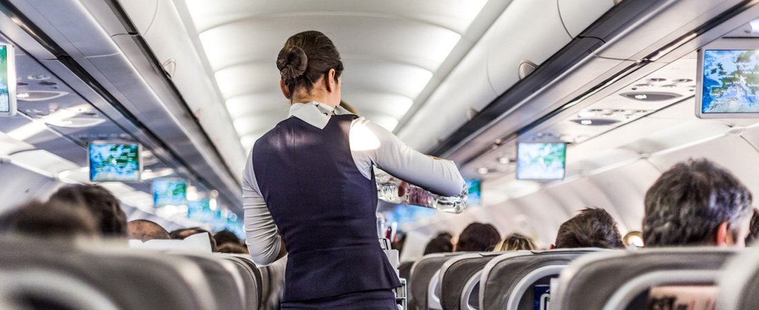 Azafata en el pasillo del avión sirviendo un vaso de agua a un pasajero durante el vuelo.